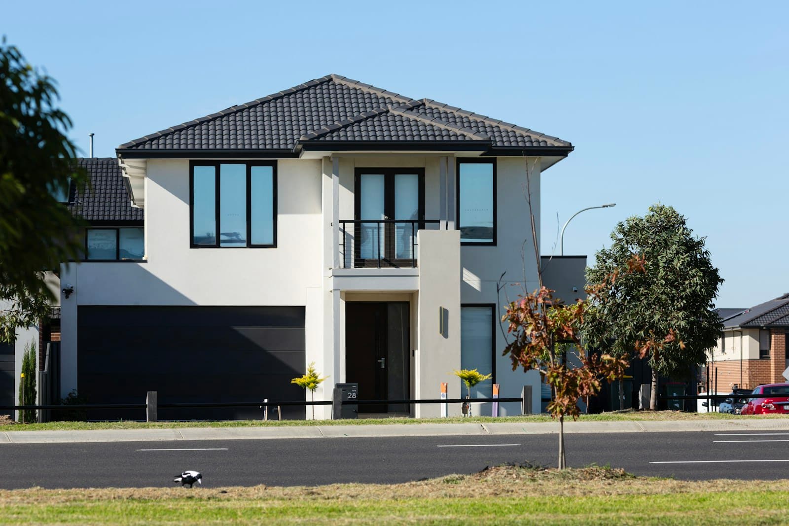 A modern two-storey house with a dark tiled roof and black-framed windows, on a suburban street.
