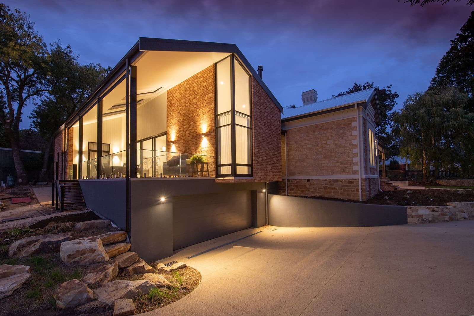 A modern brick home with floor-to-ceiling glazing and a lit driveway, at twilight.